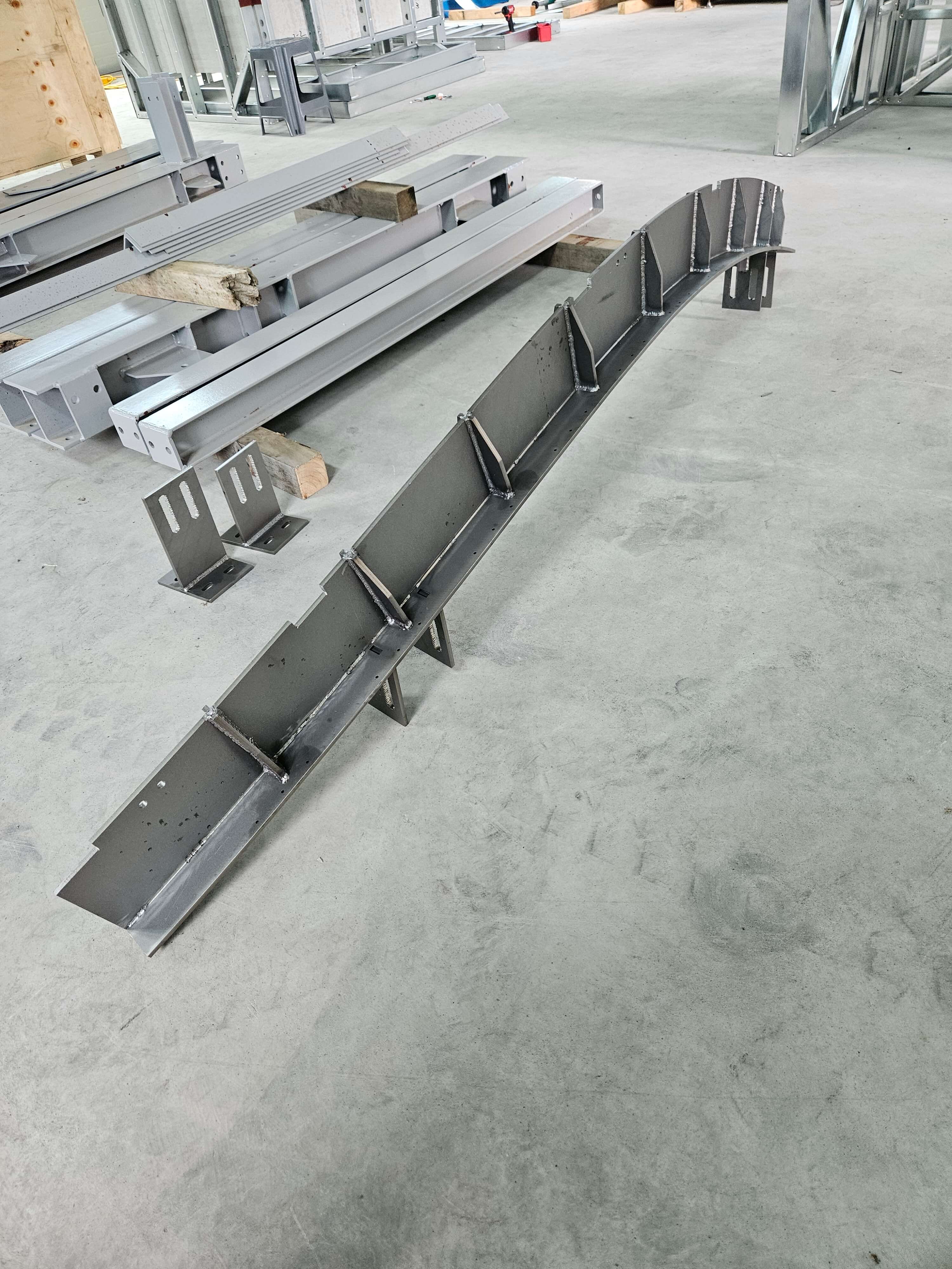 Curved gray steel member with welded brackets on the shop floor